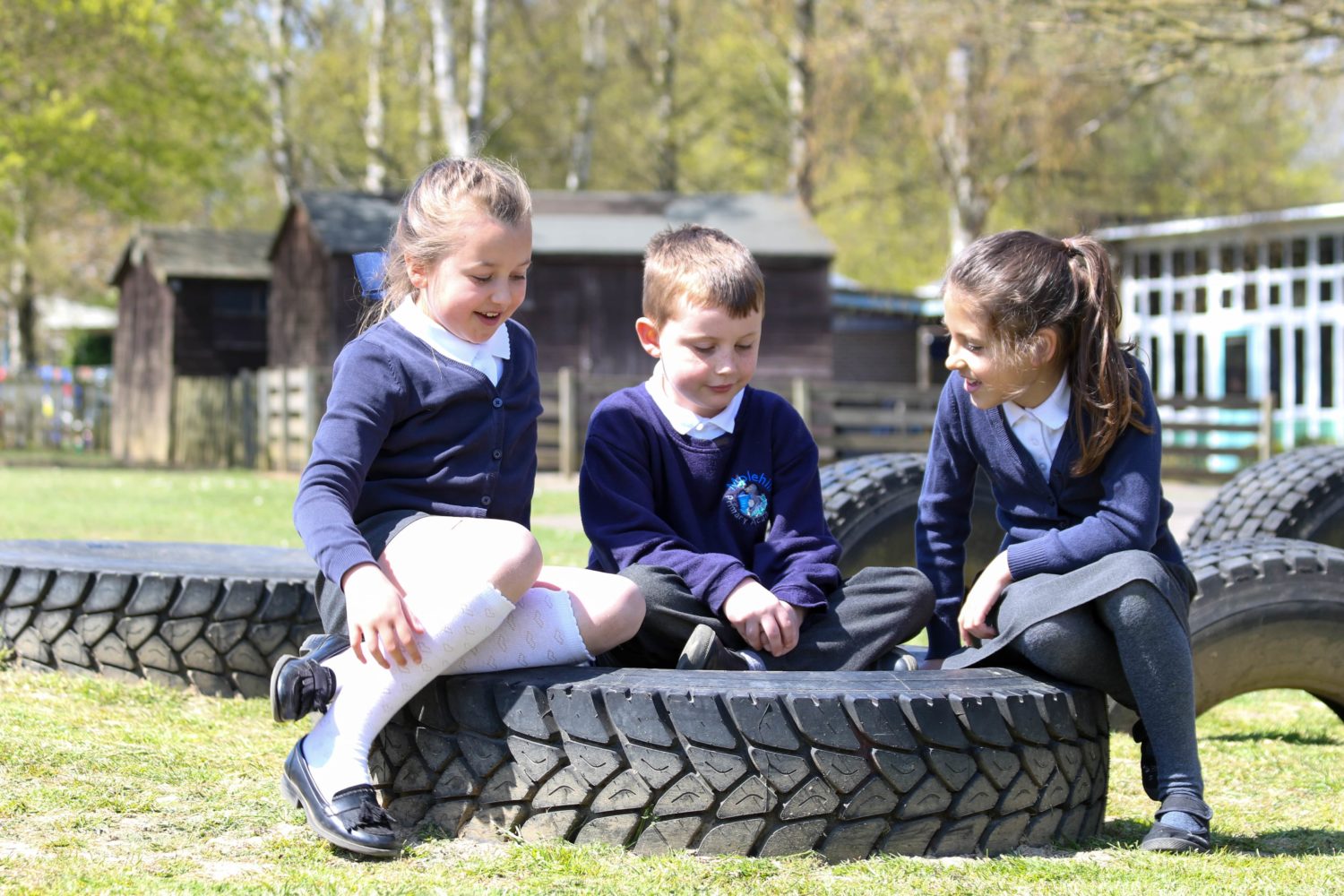 Three students sat on a tyre, conversing with one another in an outdoor area on the academy grounds.