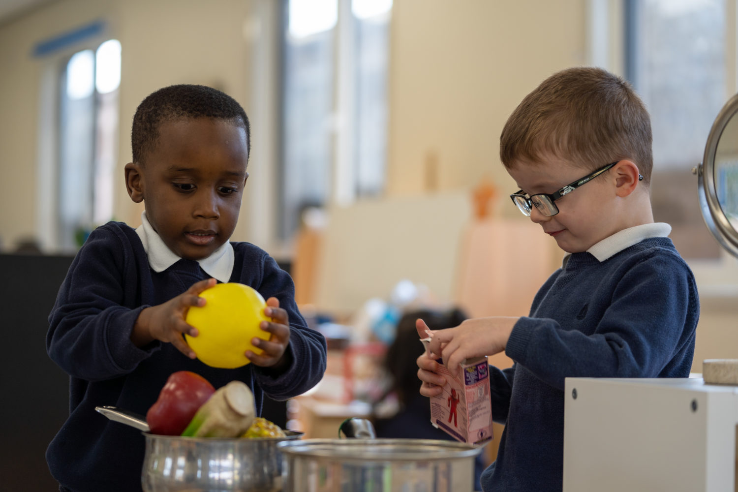 Two young boys are pictured interacting with different objects on the table in front of them. They are both wearing academy uniform.